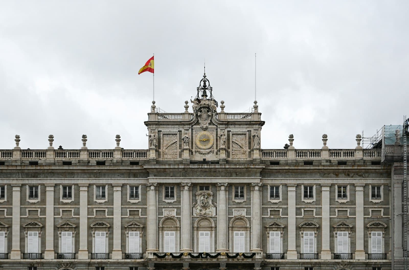 La façade du palais royal de Madrid sous un ciel gris, drapeau espagnol au sommet