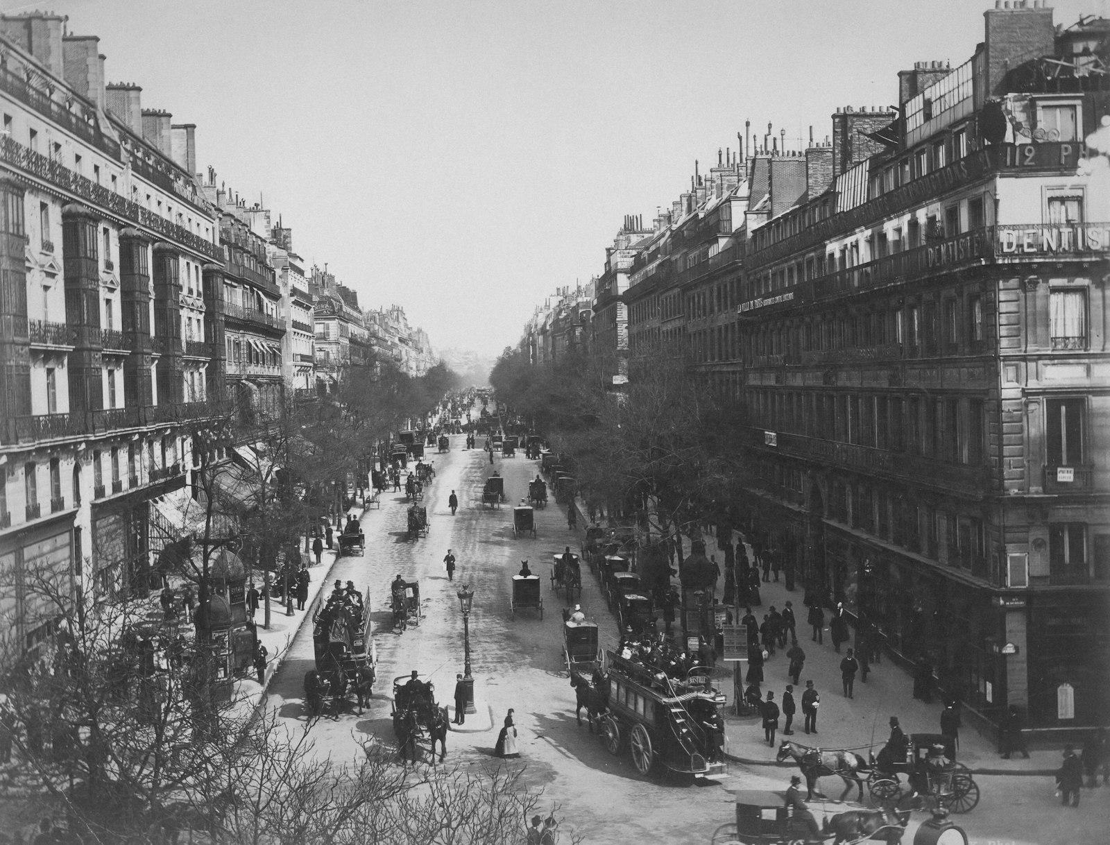 Photographie noir et blanc d'un boulevard parisien du XIXe siècle, fiacres et passants en habits d'époque