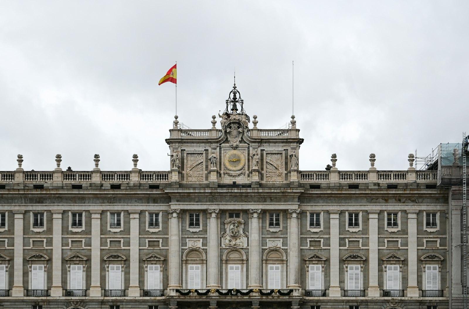 La façade du palais royal de Madrid sous un ciel gris, drapeau espagnol au sommet