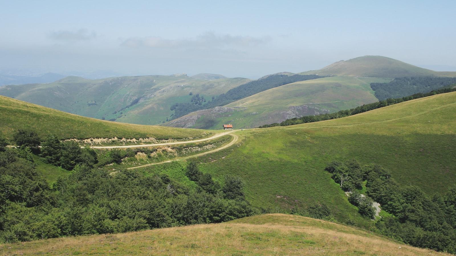 Une route sinueuse traversant les collines verdoyantes des Pyrénées sous un ciel clair
